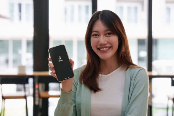 Joven mujer con gran sonrisa muestra móvil abriendo la app de Tik Tok.